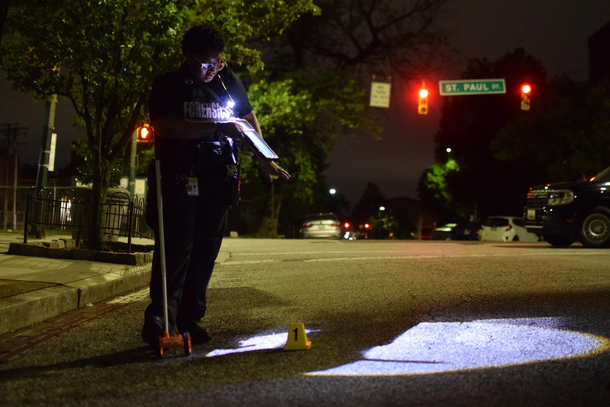 A crime lab technician measures the spot where a single cartridge casing fell following a reported shooting near the intersection of 24th Street and St Paul Street. Police began investigating the gunfire after a woman showed up at a local hospital with a gunshot wound
