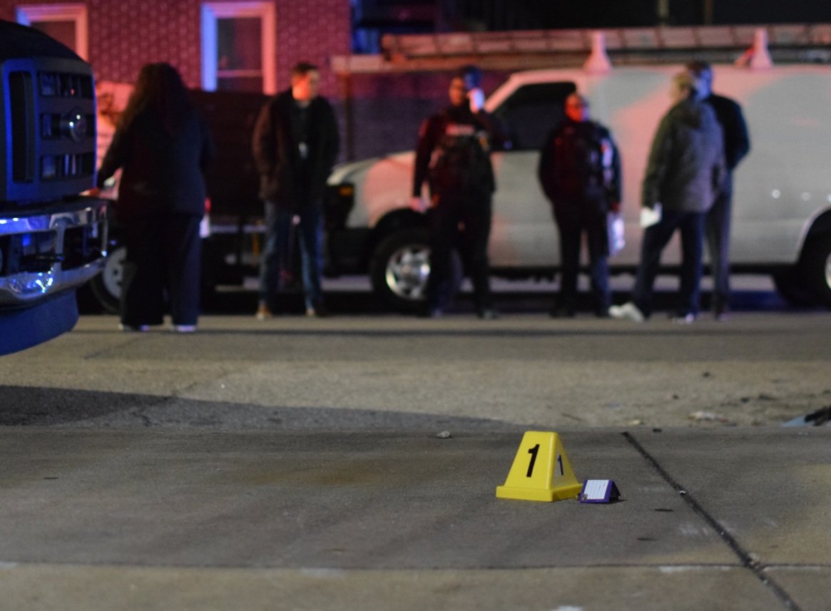 Homicide detectives and officers assigned to the Central District gather across the street from the body of a gunshot victim as crime lab technicians fly a forensics drone over the spot on the sidewalk where he was fatally shot