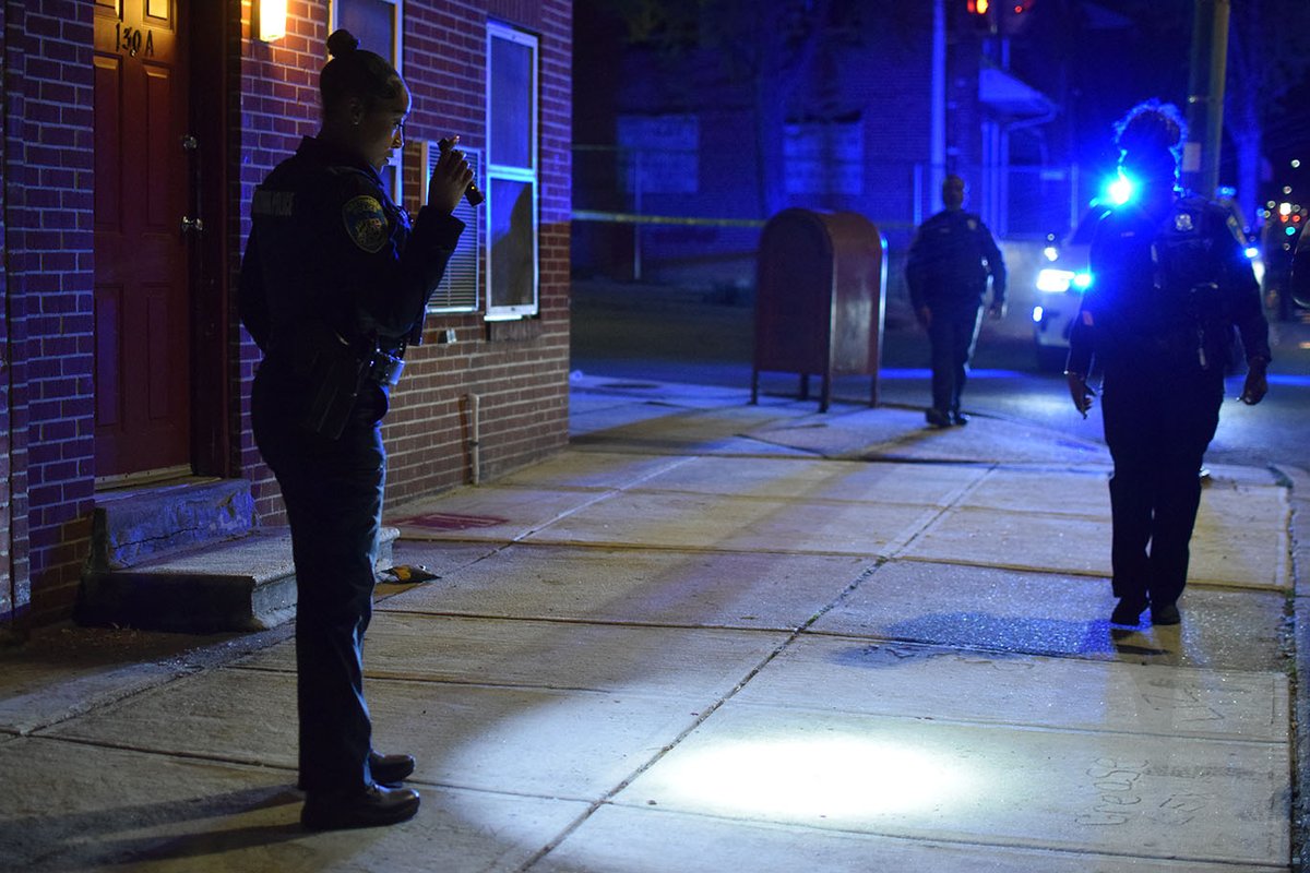 An officer examines blood spatter on the sidewalk near the intersection of West Lexington Street and North Fremont Avenue after a 51-year-old man was shot on Friday night